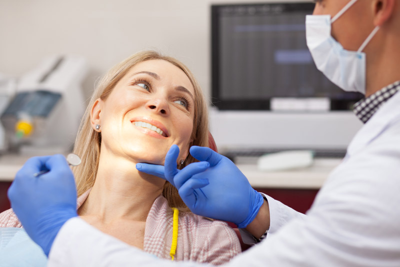 Nice lady with dark hair smiling at dentist in dental chair